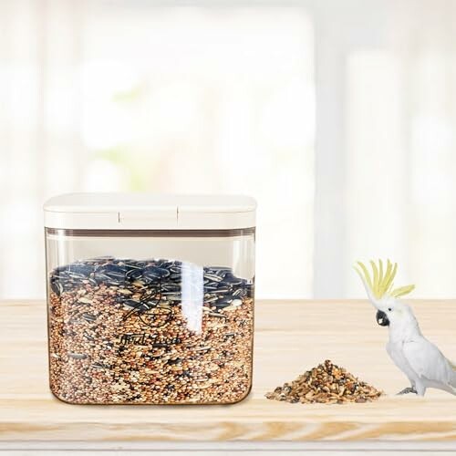 Clear container of bird seed with a cockatoo on a wooden surface.