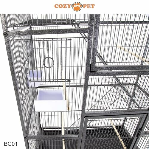 Large metal bird cage with wooden perches and feeding trays.