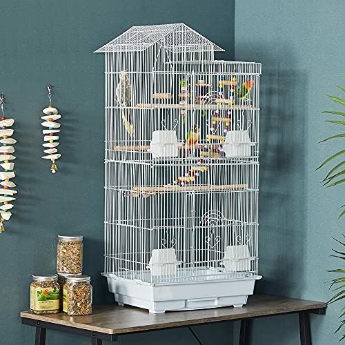 Tall white bird cage with multiple colorful birds and toys inside, placed on a table.